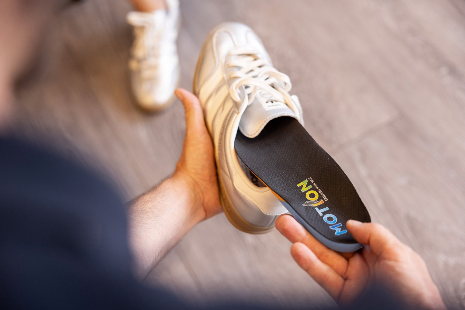 Orthopädische Einlage wird in einen hellen Sportschuh eingelegt, Hände einer MOT-Mitarbeiterin im Bild